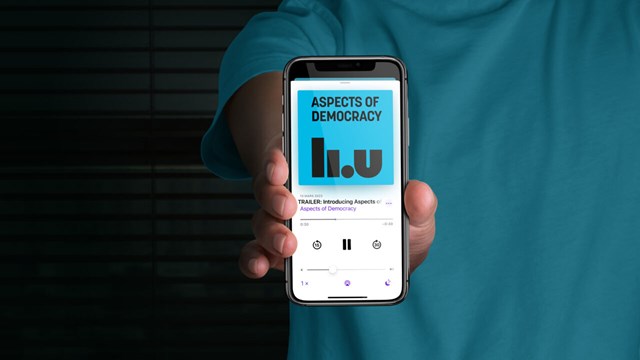 Person holding up smartphone with the podcast Aspects of Democracy on the screen.