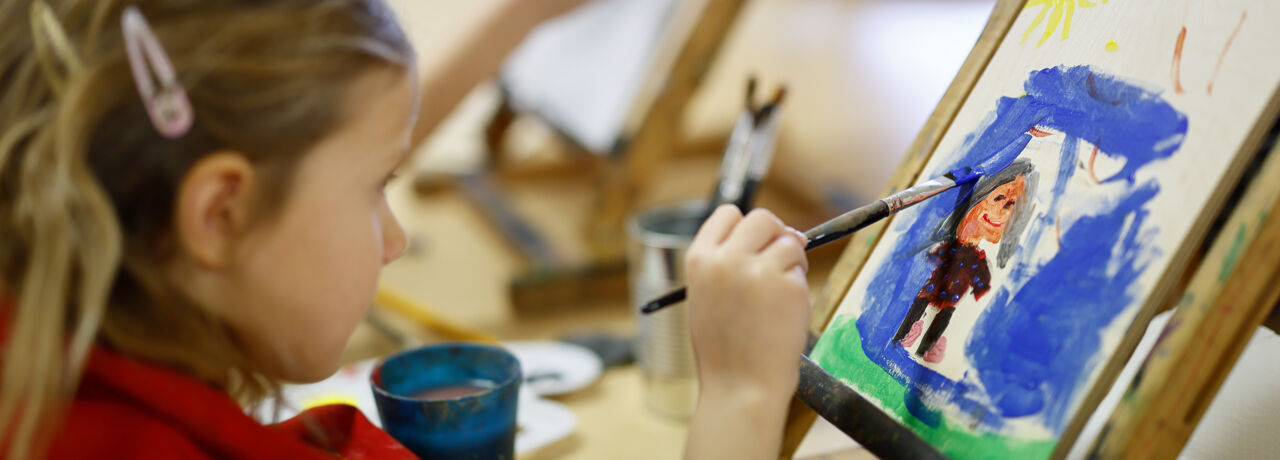 Ett barn sitter och målar med oljefärg.
