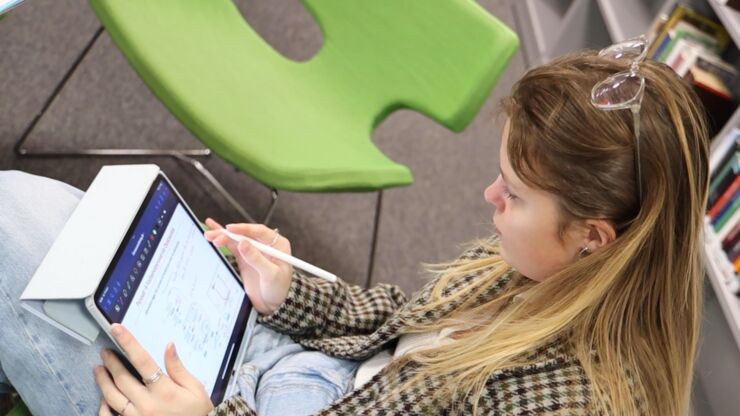 Student sitter och studerar med en surfplatta i biliotek.