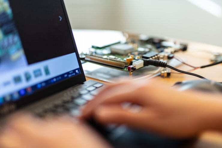 Händer på en laptops tangentbord, i bakgrunden ett kretskort