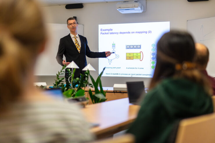 Students listening to a teacher pointing to an example at a big screen.