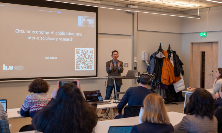 En man stands in front of people and presents  his research.