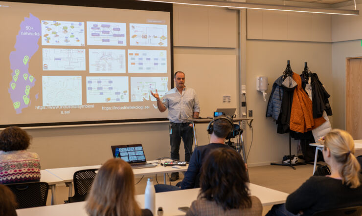 En man stands in front of people and presents  his research.