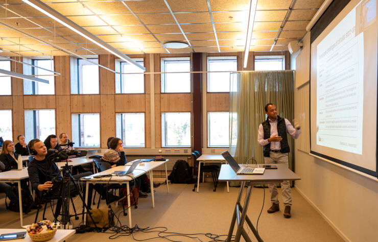 En man stands in front of people and presents  his research.