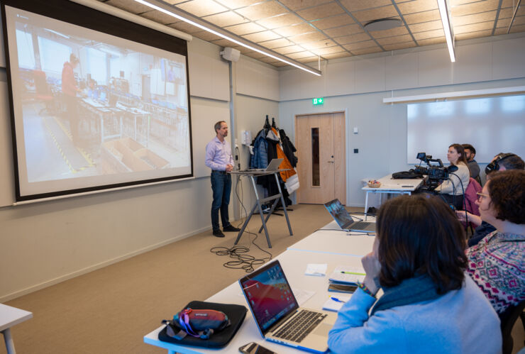 En man stands in front of people and presents  his research.