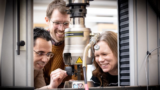 Three researchers by machine that is testing strength in materials.