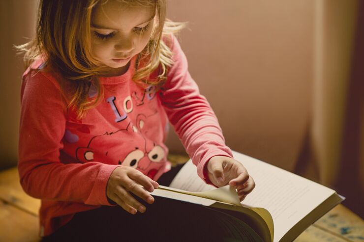 Flicka i rosa tröja bläddrar i en bok. 