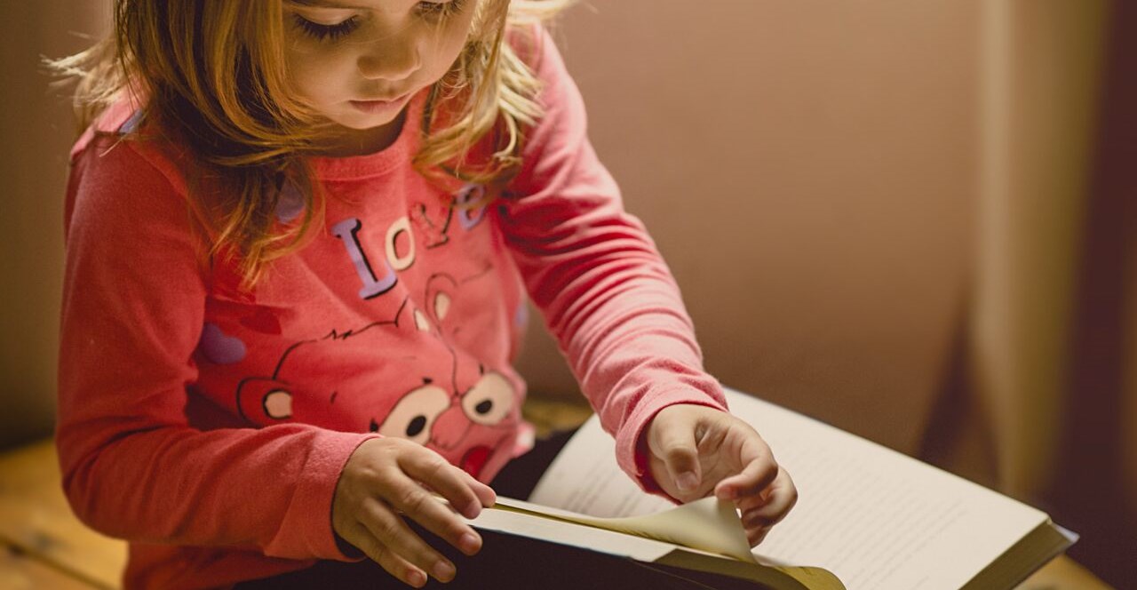 Flicka i rosa tröja bläddrar i en bok. 