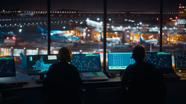 Två flygledare framför en rad med datorskärmar i flygledartorn på natten.