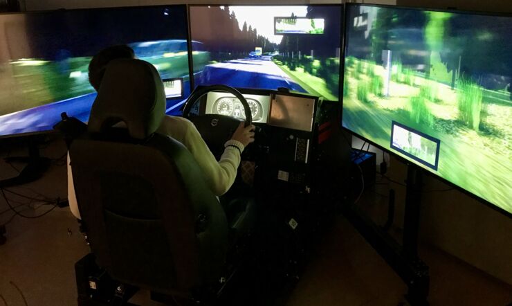 En person sitter med händerna på ratten framför en körsimulator