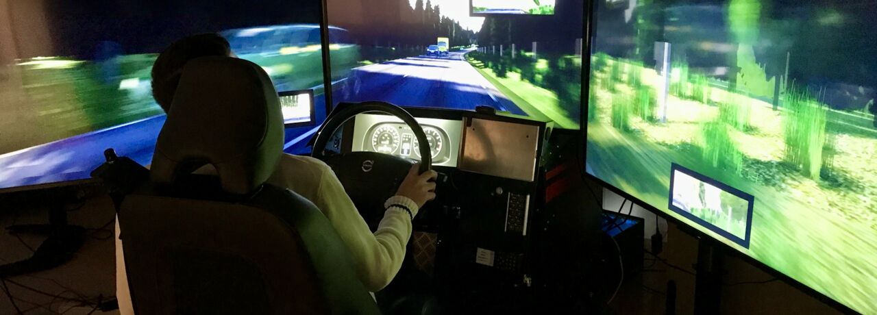 En person sitter med händerna på ratten framför en körsimulator