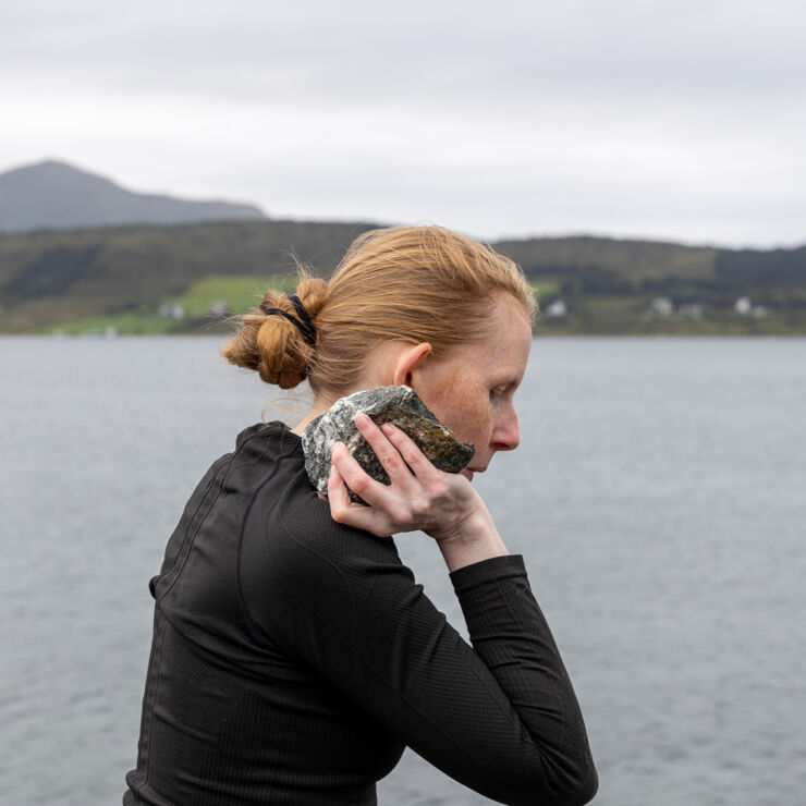  Tina Mariane Krogh Madsen stands by a lake and holds a large stone like a shot putter.