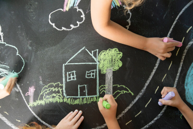 Barn som ritar hus, träd, bilar med tavelkritor