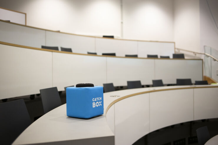 Rows of dark chairs in a bright lecture hall with a blue box lying on one of the benches.