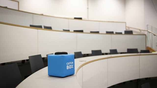 Rows of dark chairs in a bright lecture hall with a blue box lying on one of the benches.