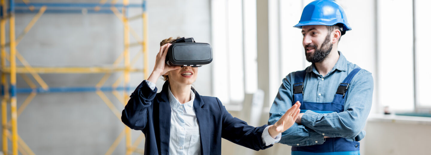 Woman client wearing VR glasses imagining future interior standing with builder at the construction site-