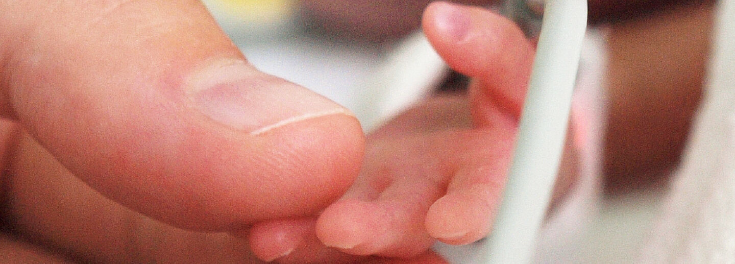 An adult's hand holds the hand of a premature baby.