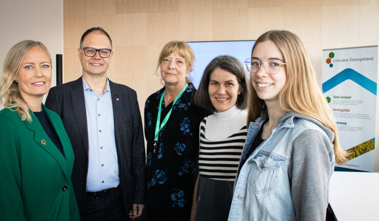 grupp, fyra kvinnor och en man framför affisch.