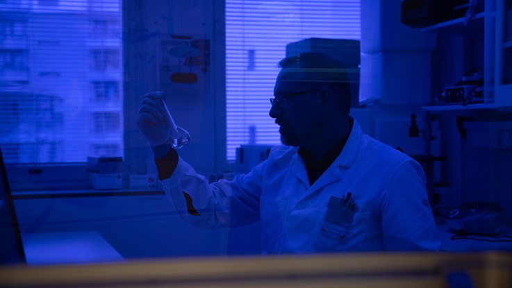 Manlig forskare i labbmiljö med blå bakgrund.