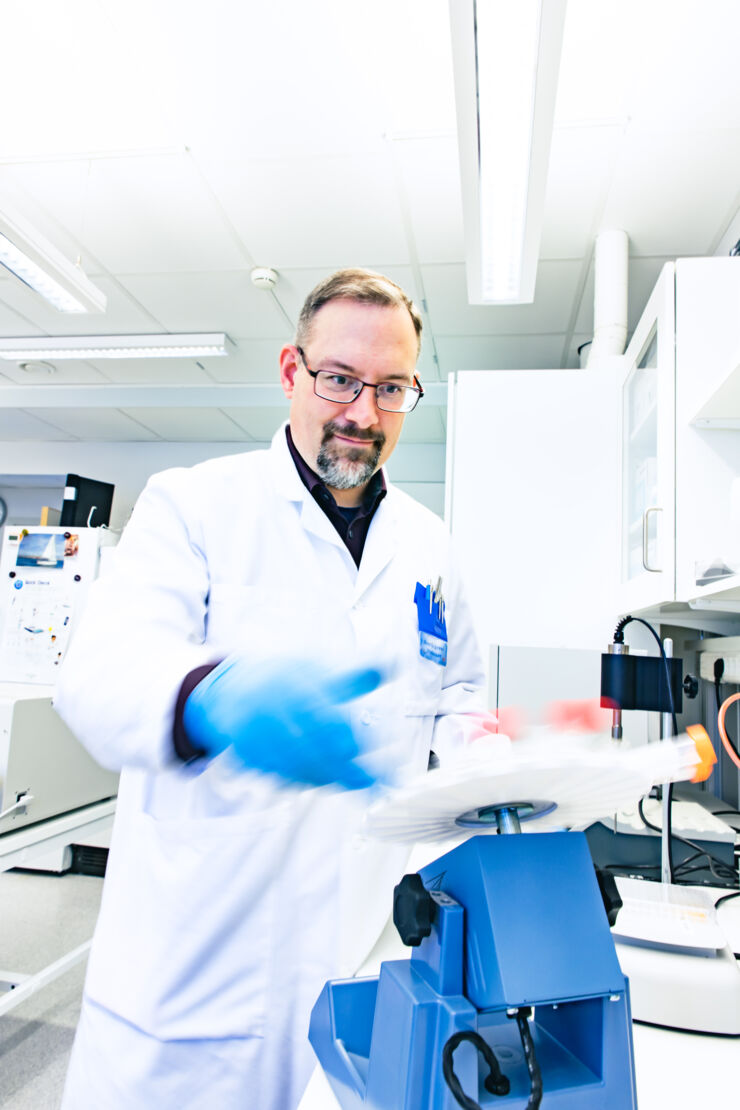 Man i vit labbrock hanterar prover på labb.