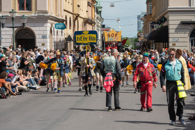 Orkester i gula jackor går längs gata omgiven av folk