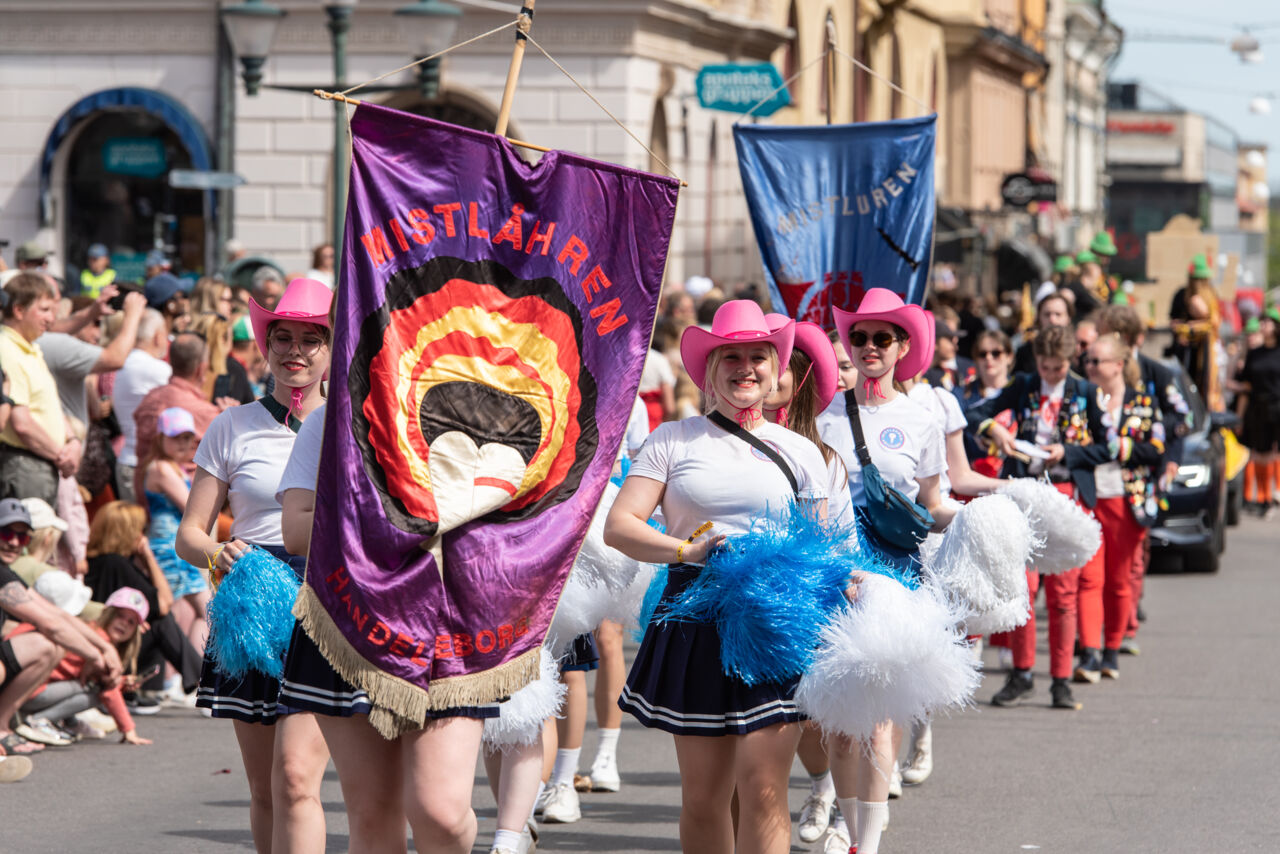 Young women holding pompoms walk along a street in the sun