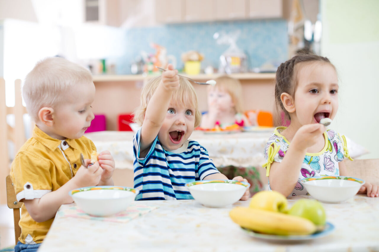 Three kids eating on a pre-school.