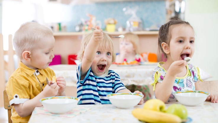 Three kids eating on a pre-school.