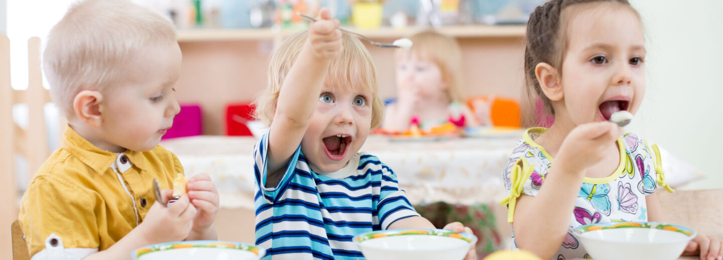 Three kids eating on a pre-school.