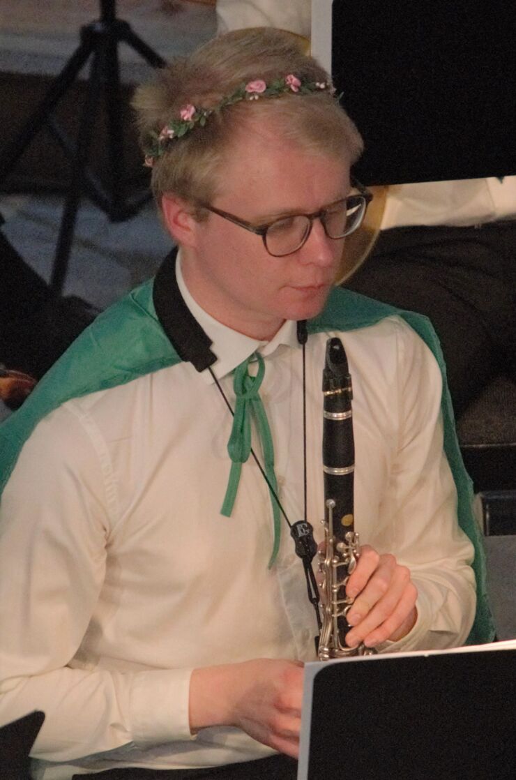 Niklas Hamström spelar klarinett klädd i hårband av blommor och en cape över axlarna
