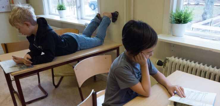 Two boys in a classroom reading books.