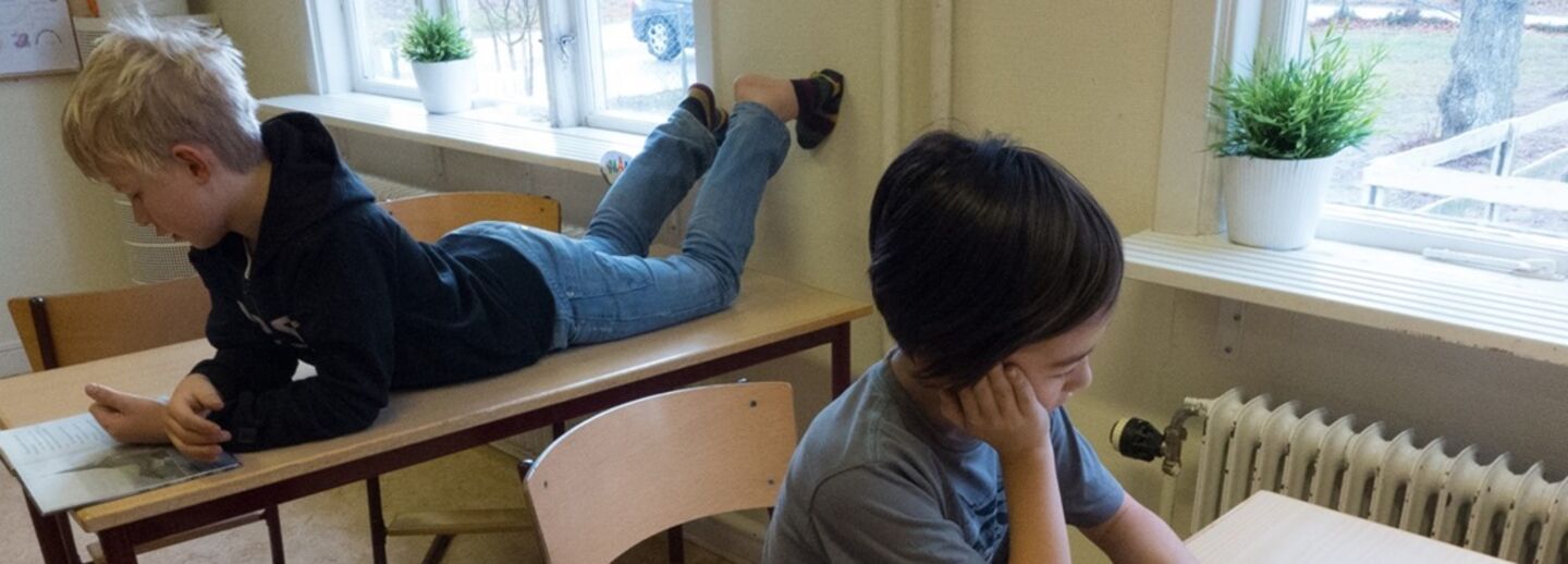 Two boys in a classroom reading books.