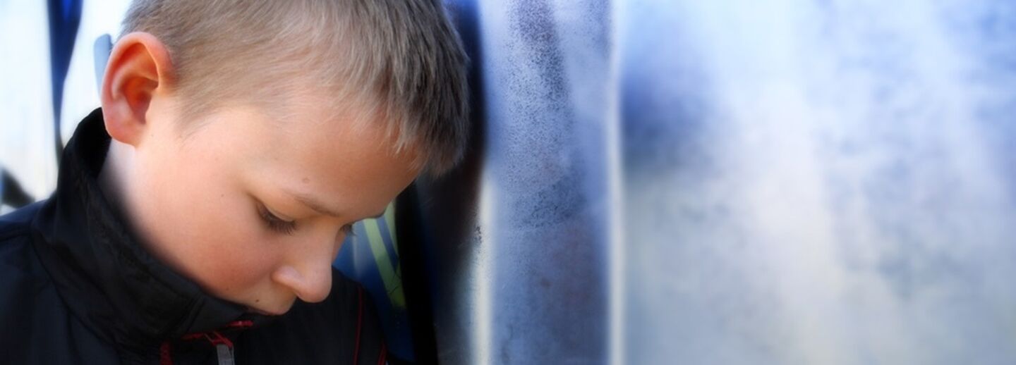 En ensam pojke står lutad mot en vägg.