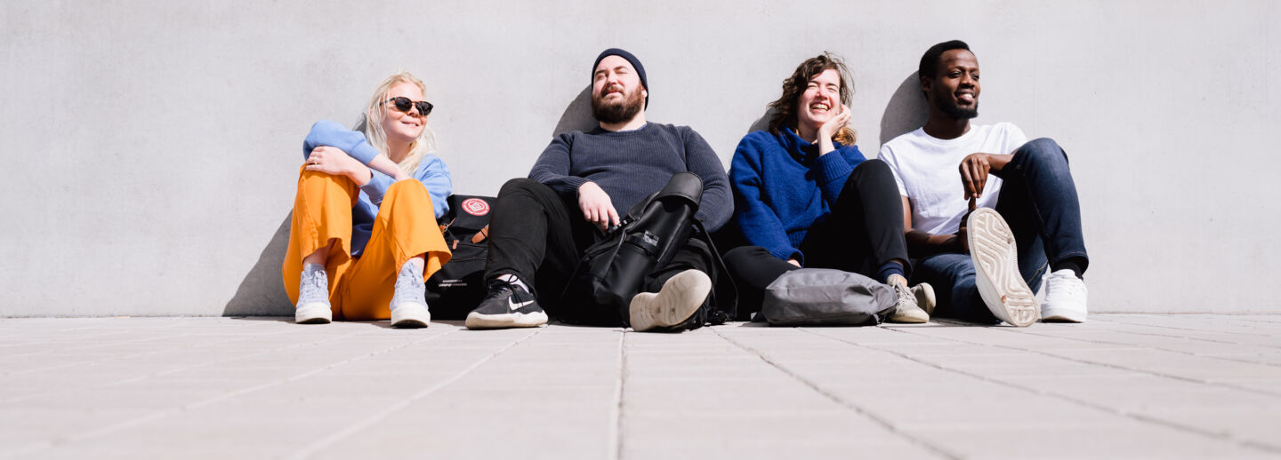 Four people sit against a wall outdoors