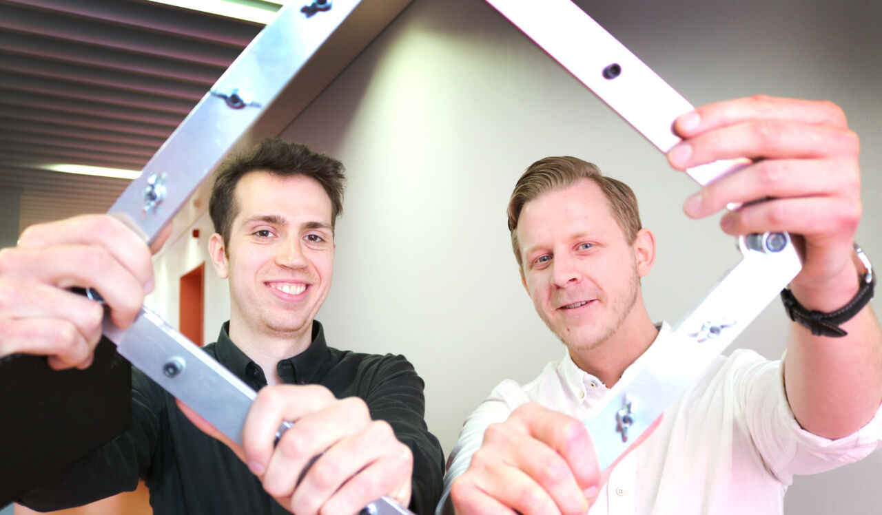 Två manliga studenter håller i fyrkantig modul av metall.