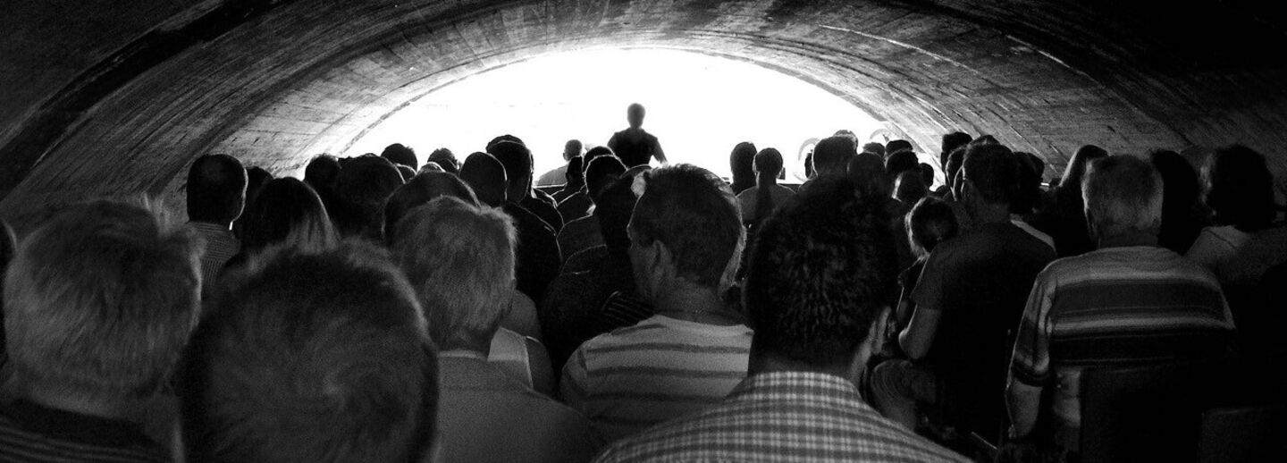 A group of people sitting in a dark room listning to a speaker.