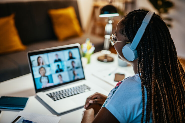 A woman with headphones and computer sitting in a Zoom meeting.