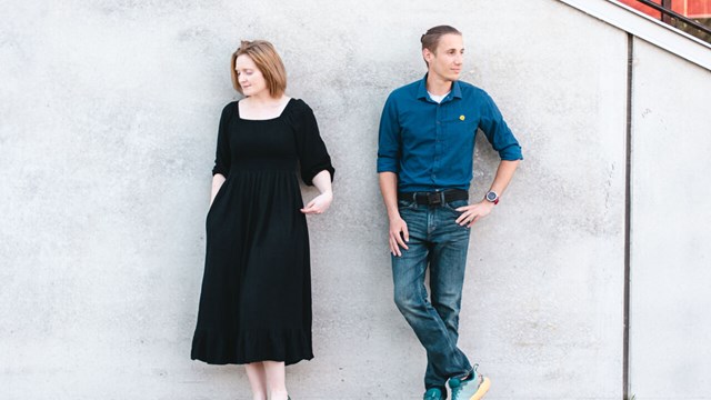 Alice Langley and Jean-Pierre Roux is standing by a concrete wall.