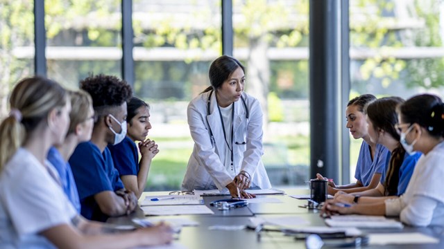 a group of medical students sit around a table and discuss. 