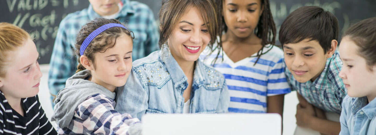 A teacher and a group of children looking at a computor.