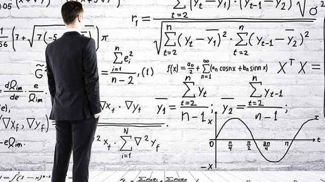a man in a suit looks at a board with different formulas.