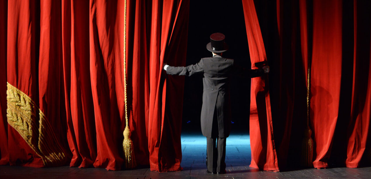 A man in a tuxedo opens a red curtain.