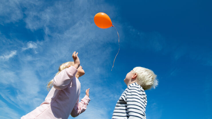 Flicka och pojke tittar upp mot ballong i himlen