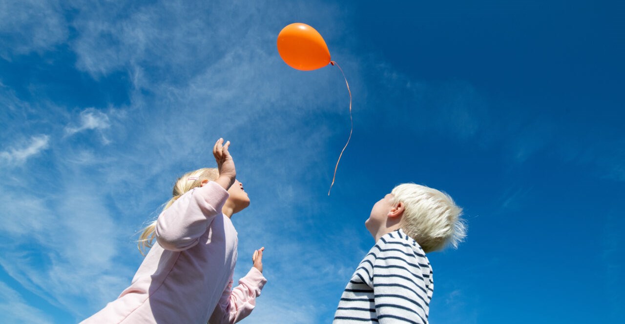 Flicka och pojke tittar upp mot ballong i himlen