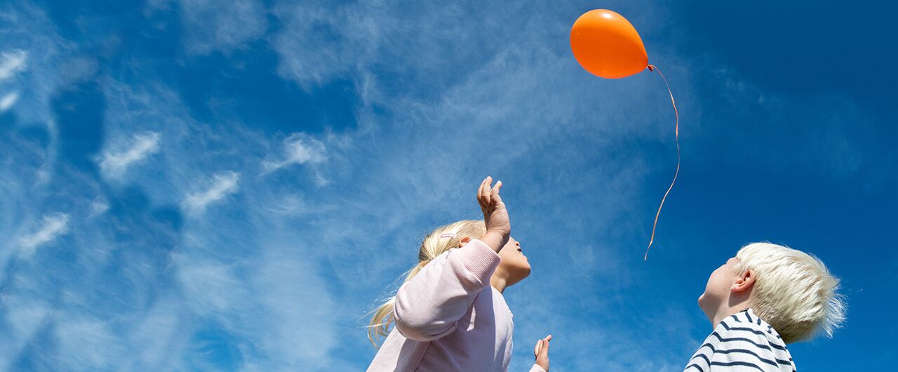 Flicka och pojke tittar upp mot ballong i himlen