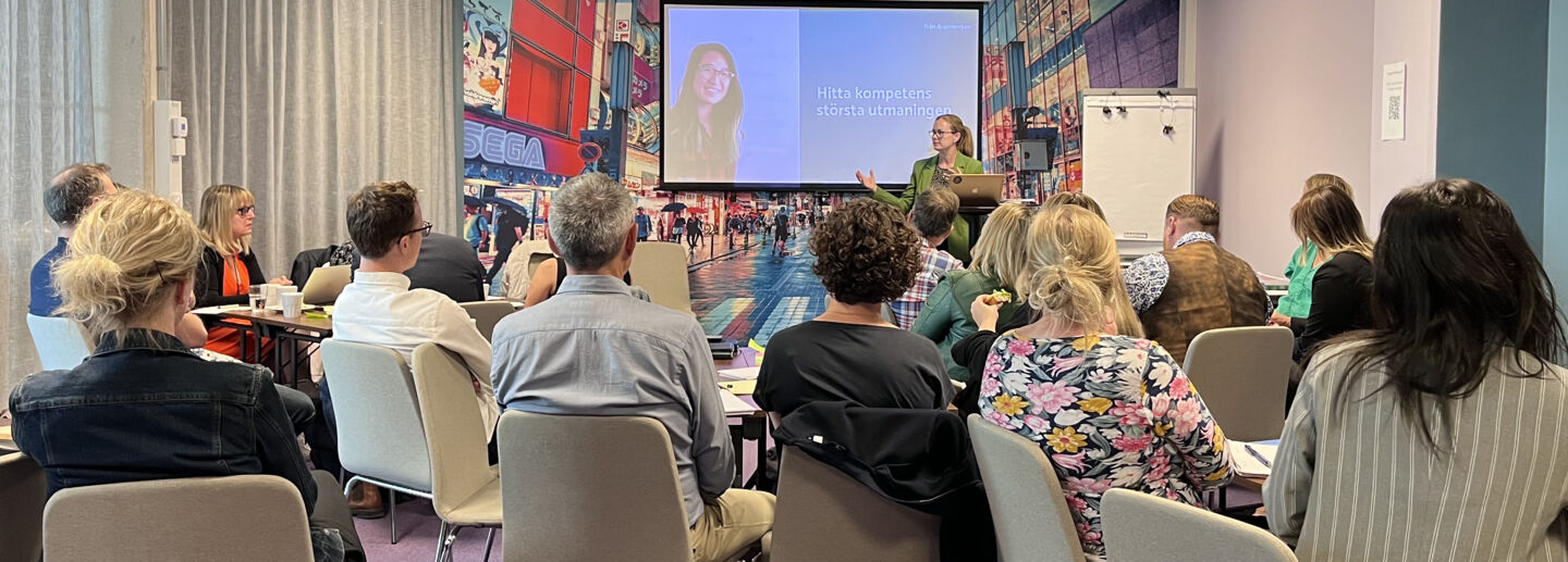 Människor sitter i ett rum och lyssnar på en föreläsare.