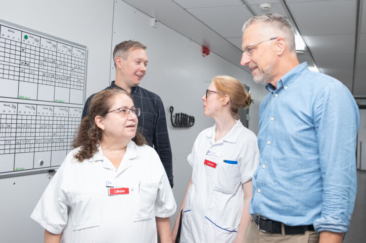 Two women in hospital wear and two men talk in a corridor.