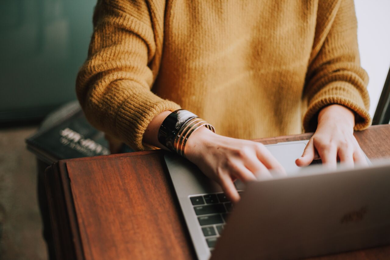 Person wearing a colourful jersey typing on laptop.