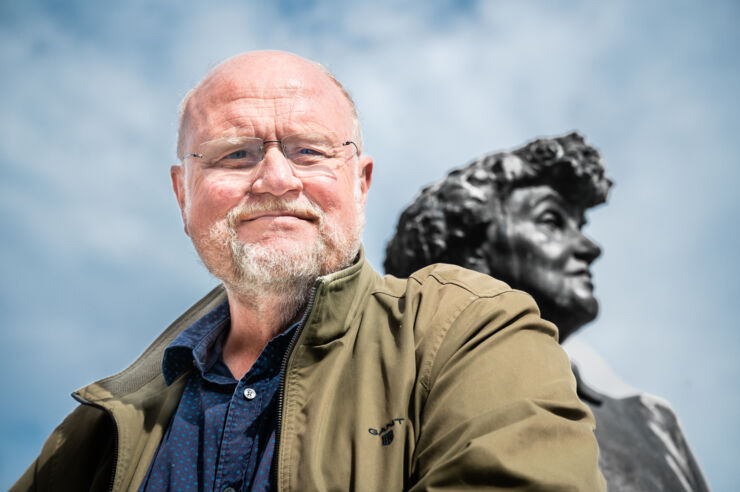 Portrait of Ola Larsmo against a blue sky and the Moa Martinson sculpture in the background.