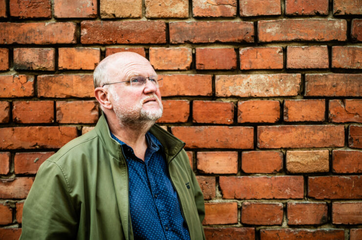 Portrait of Ola Larsmo against a wall.